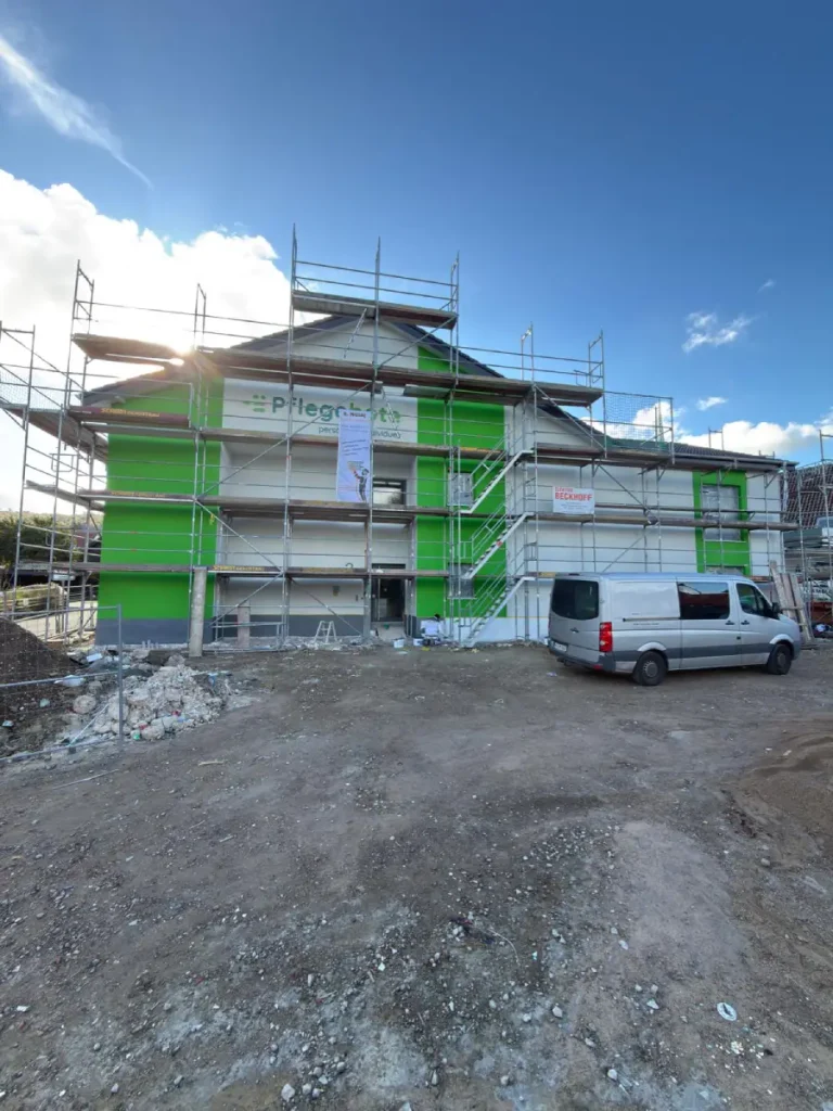 Gesamte Frontansicht eines aufgestellten Gerüsts an einer Außenwand, mit Firmenfahrzeug davor.