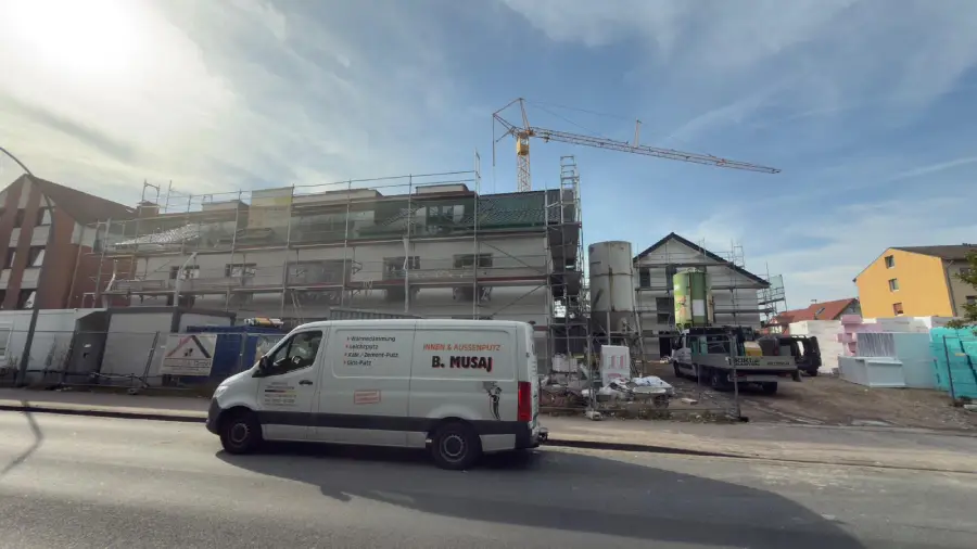 Aufgestelltes Gerüst an einer Außenwand, während der Außenputz arbeiten. Weitansicht mit Firmenfahrzeug.