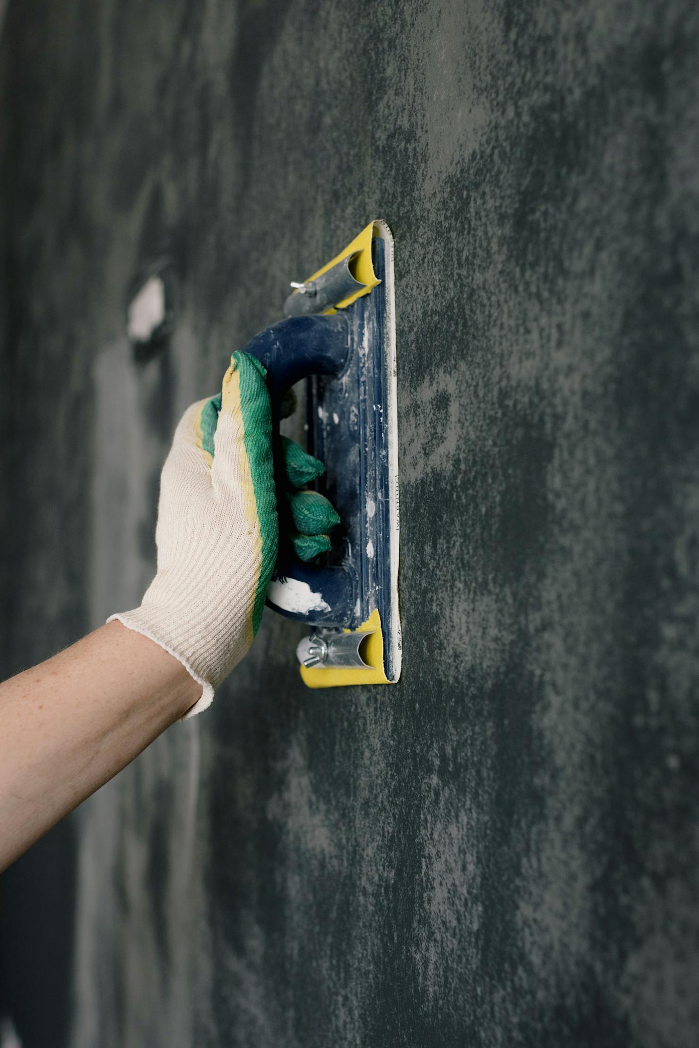 Arbeiter mit Handschuhen, der einen Spachtel hält und die Wände in einer Wohnung ausgleicht.